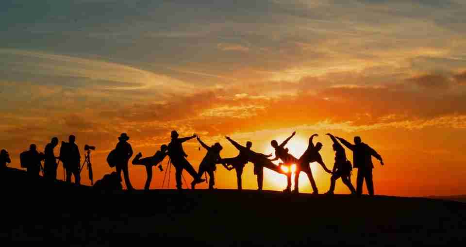 group silhouette in front of orange sunset, team building