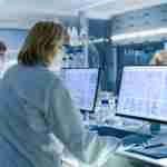 Female and Male Scientists Working on their Computers In Big Modern Laboratory. Various Shelves with Beakers, Chemicals and Different Technical Equipment is Visible.