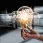 Hand holding light bulb and cog inside. Idea and imagination. Creative and inspiration. Innovation gears icon with network connection on human heads on metal texture background. Innovative technology in science and industrial concept